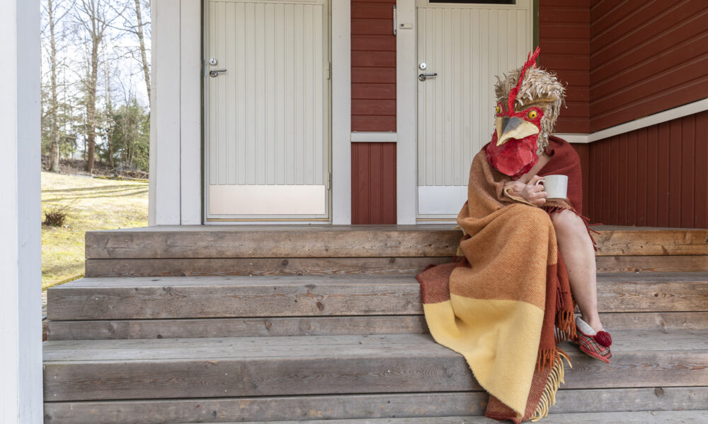 The Chicken sitting on the porch wrapped in a blanket holding a coffee cup.